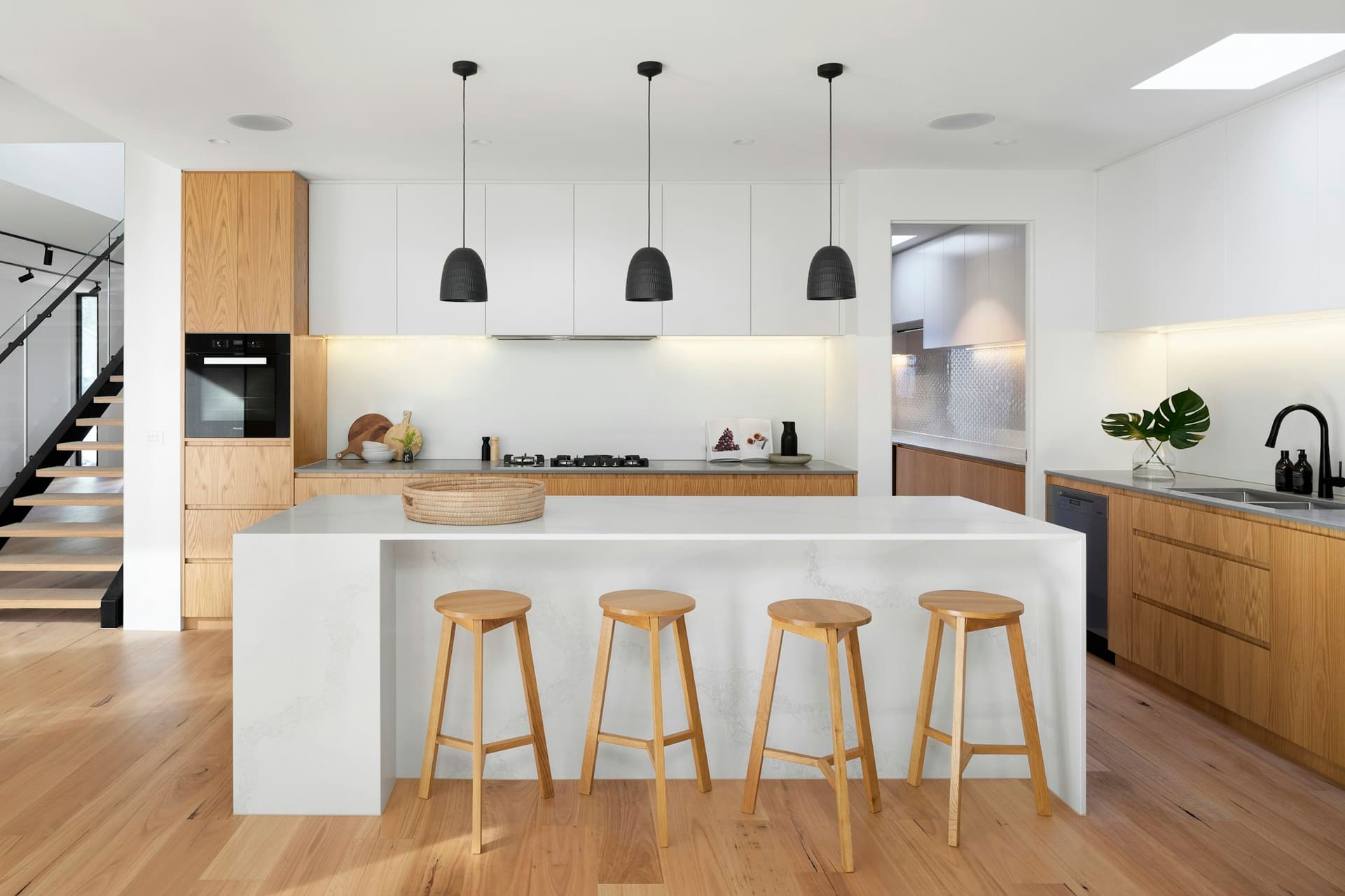A white kitchen island with four oak stools under black pendant lights, oak cabinetry running along the back wall.